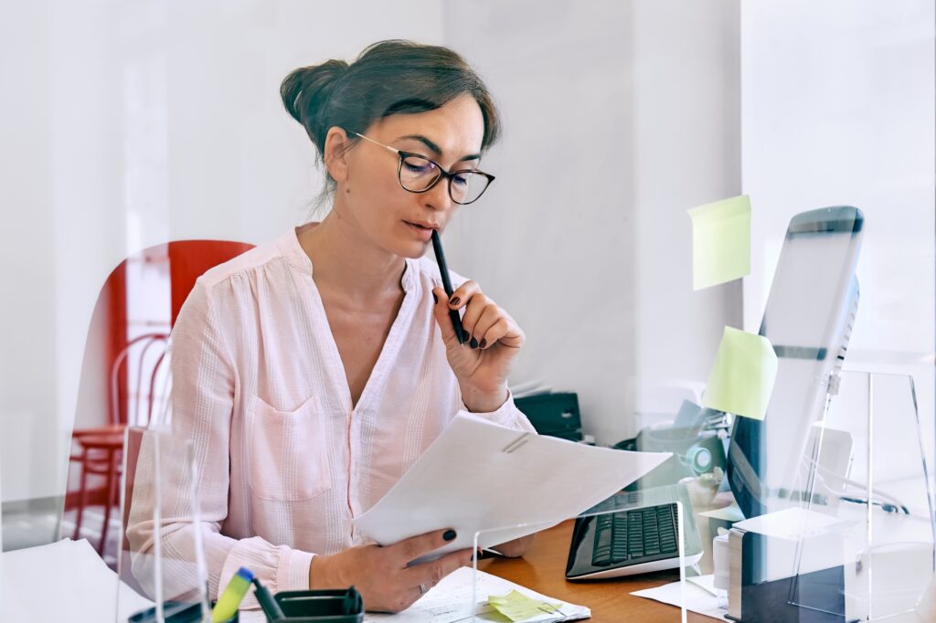 Focused professional reviewing financial documents at her desk, illustrating the accuracy and diligence businesses seek when they hire bookkeepers for support.