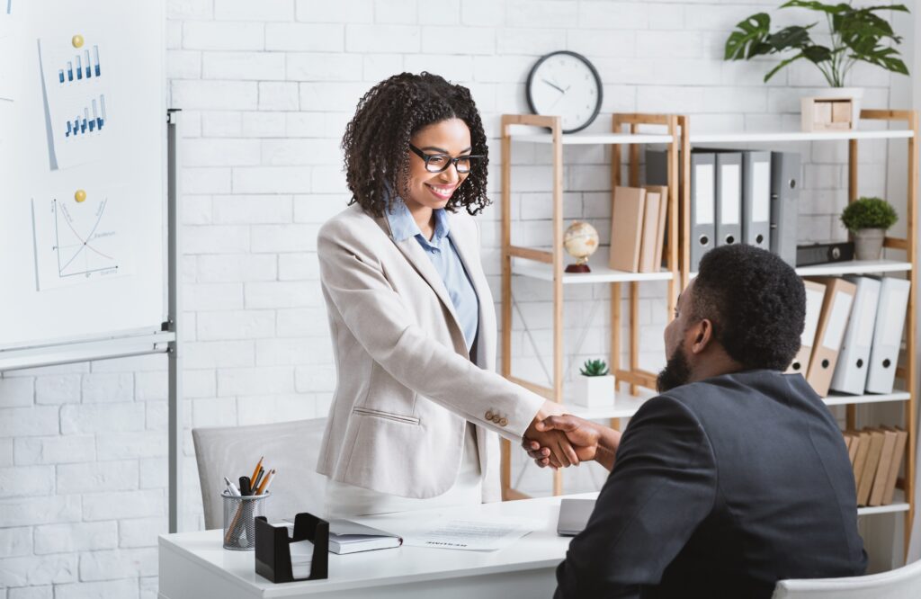 Business professional shaking hands with a job candidate in a modern office, illustrating successful placement through a temporary staffing agency.