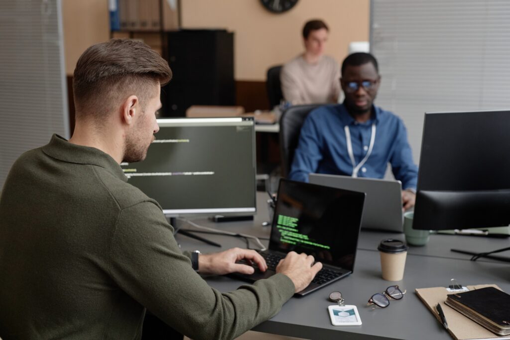 Software engineers collaborating in a modern office while working on laptops with code, illustrating a productive tech team environment enabled by remote IT staffing solutions.