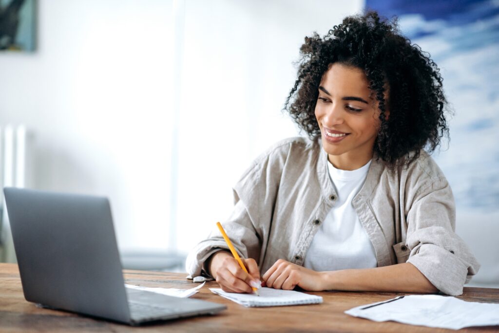 Smiling woman taking notes while watching a laptop—capturing a remote learning moment that reflects actionable job seeker advice from recruiters for career growth. 