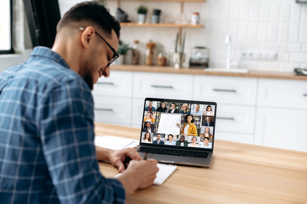 Man attending a virtual meeting and taking notes from a video call—demonstrating best practices on how to hire remote workers and manage distributed teams effectively. 
