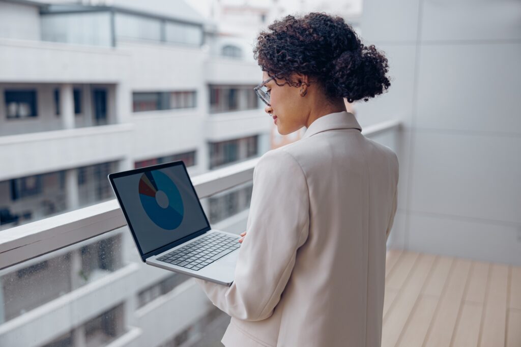 Businesswoman analyzing financial data on a laptop from an office balcony, representing top talent sourced through an accounting staffing agency.
