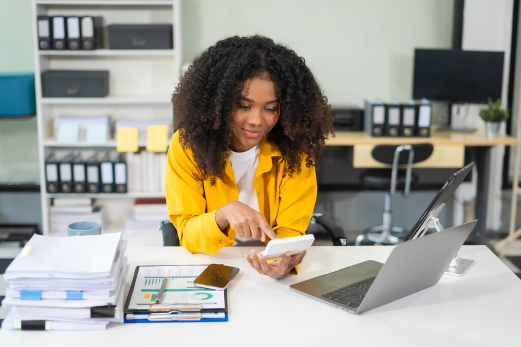 Smiling professional reviewing financial data at her desk with a phone and laptop, representing the precision and support offered by CPA staffing services. 