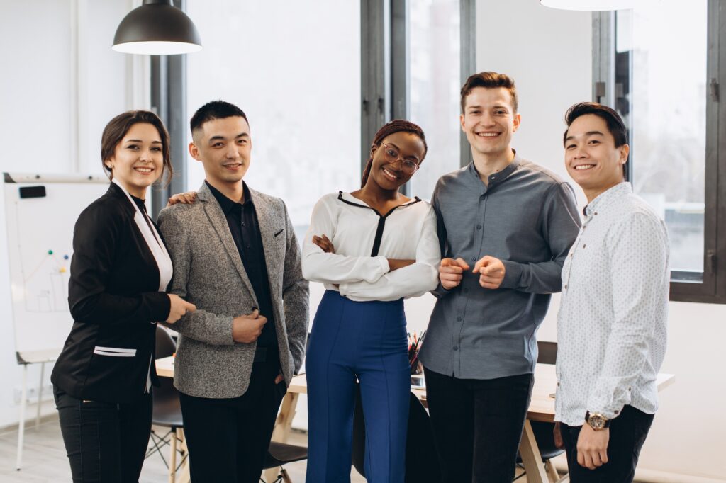 Diverse team of professionals posing confidently in a modern office—capturing workplace trends and collaboration highlighted in today’s staffing industry insights. 