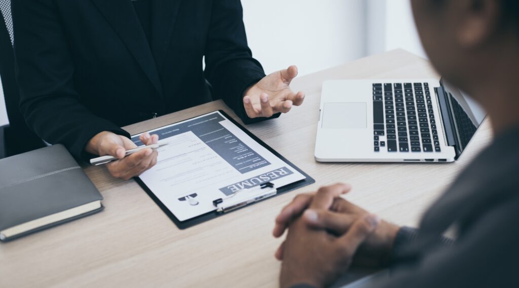 HR professional discussing a resume during an interview to hire top talent, with a candidate seated across a modern desk featuring a laptop and documents.