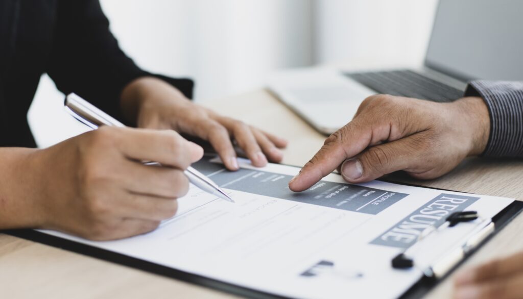 Close-up of a recruiter reviewing a resume and discussing qualifications during a hiring process, representing professional temporary staffing services in a corporate setting.