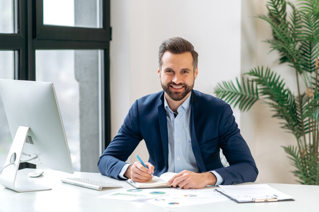 Confident professional at a modern desk smiling at the camera—representing business agility, strategic planning, and insights driven by temp staffing market trends. 