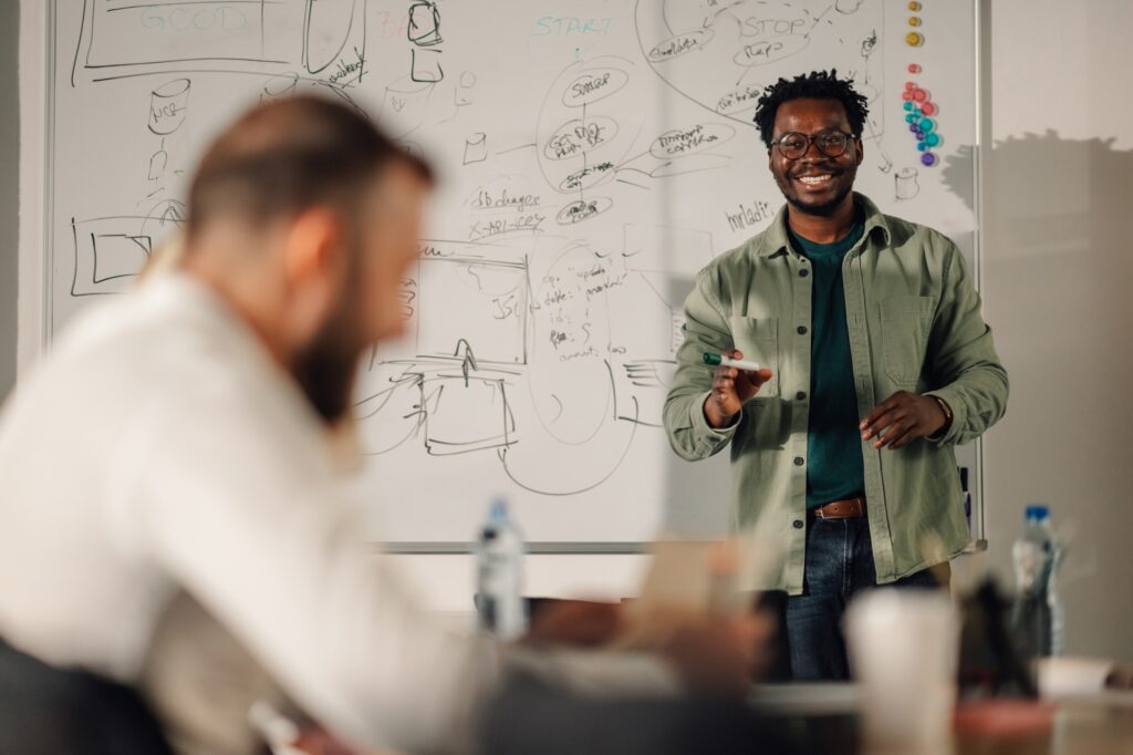 Team meeting led by a tech professional presenting on a whiteboard, symbolizing the collaborative innovation supported by a tech staffing agency in sourcing top-tier IT talent.