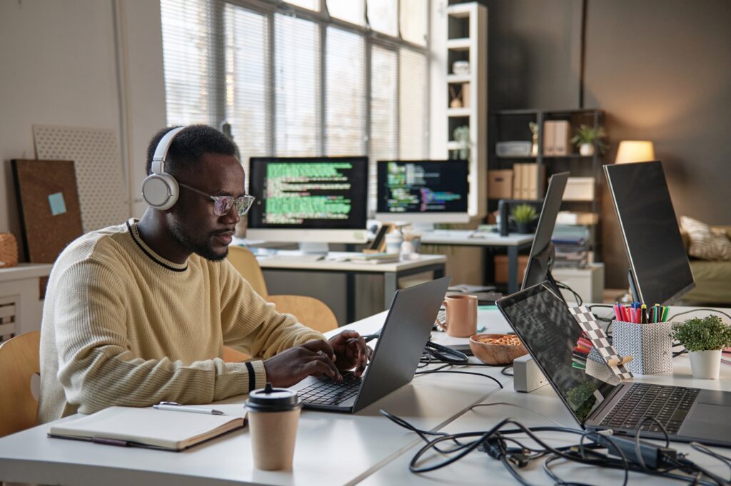 IT staffing services professional working on multiple laptops in a modern office, analyzing code and collaborating on tech solutions in a corporate workspace. 