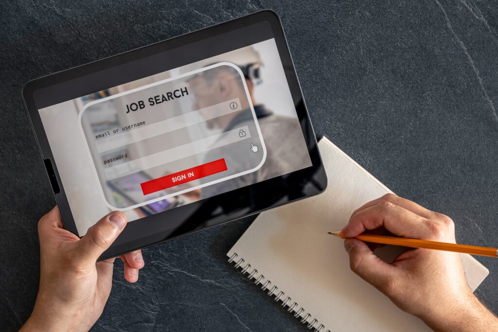 Person holding a tablet displaying a job search login screen while taking notes on a notepad, representing a professional approach to a personalized job search experience.
