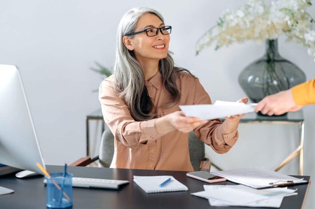 Professional woman in an office handing over documents with a smile, symbolizing efficient and personalized staffing solutions for business operations.